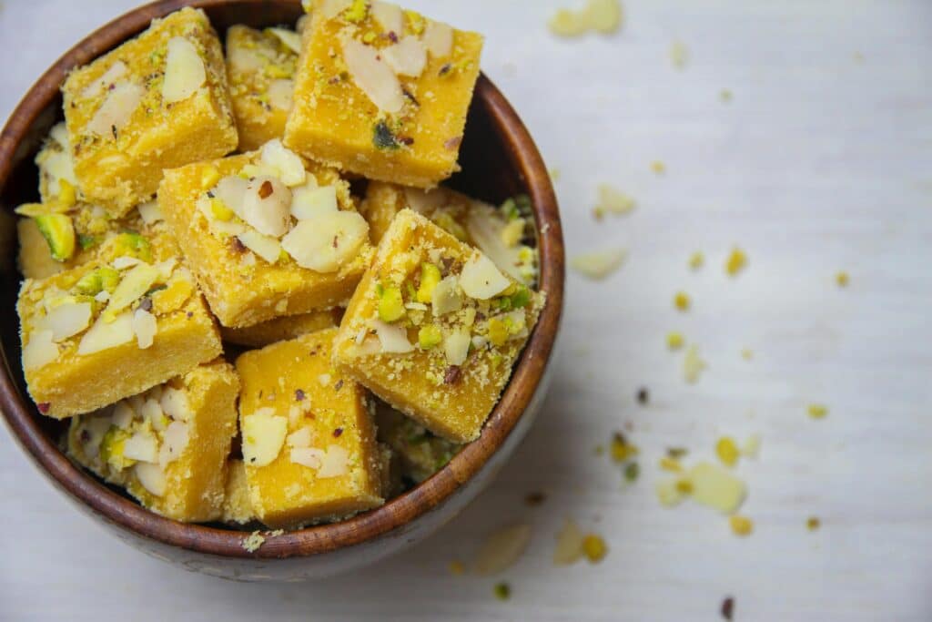 Top view of delicious Indian besan barfi garnished with almonds and pistachios, served in a wooden bowl.